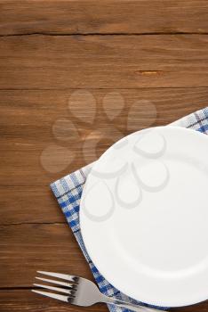 white plate and fork at napkin on wooden background