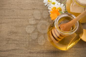 jar of honey and flowers on wood background