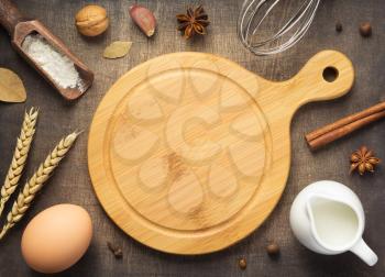cutting board and bakery ingredients on wooden background, top view