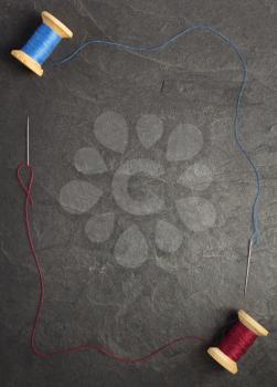 spool of thread and needle on slate stone background, top view