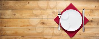 plate, knife and fork at rustic wooden plank board table background, top view