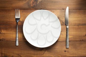 plate, knife and fork at wooden background texture, top view