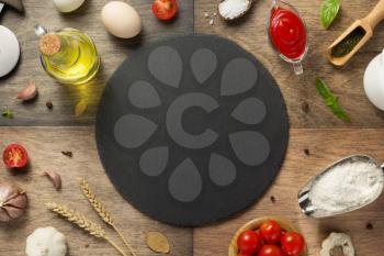 pizza food ingredients and slate stone cutting board at wooden table, top view