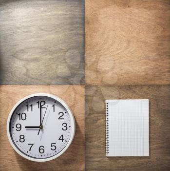 checked notebook and wall clock at wooden background