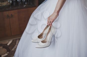 The hand of the woman holds white shoes.