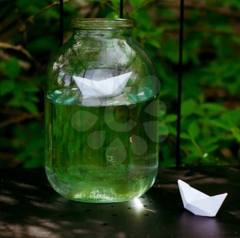 Paper ships in bank. Bank costed in a shade of a bush in the street in a garden.
