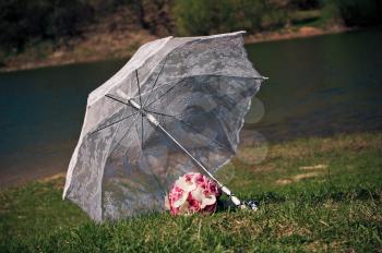 Umbrella and bouquet.
White transparent umbrella and wedding bouquet on river bank.
