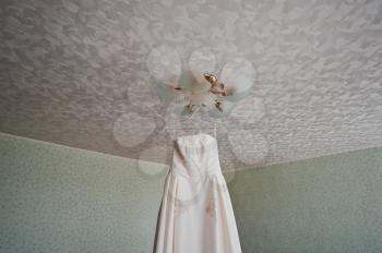 The wedding dress hangs in a room.