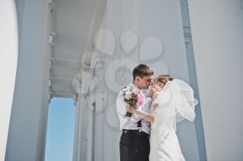 The groom embraces the bride with the white columns.