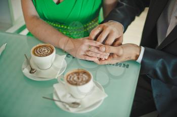 Hands of the woman embracing hands of the man on a table with cups of coffee