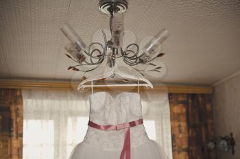 The white beautiful wedding dress hangs on a chandelier.