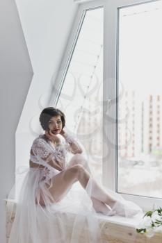Portrait of a girl in a negligee on background of the window.