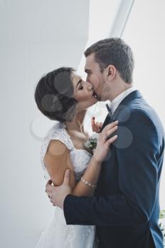 Young husband and wife gently kiss each other on the bright background of the window.