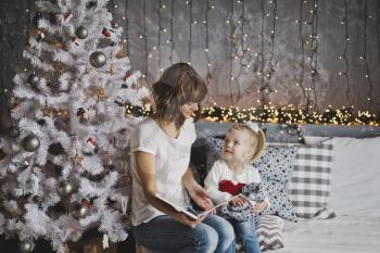 Mother year-old daughter read the book in Christmas decorations.