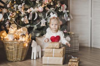 Little girl sitting under the Christmas tree with gifts.