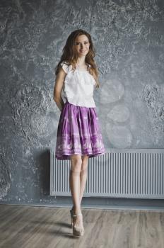 A life-size portrait of a girl in a skirt and with long hair on grey background textured wall.
