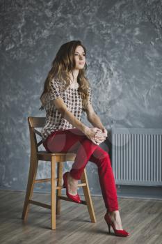 Young girl in red jeans was sitting on a chair.