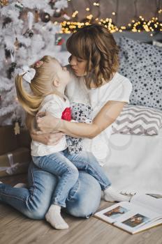 Family hug of a mother and daughter in front of a Christmas tree.