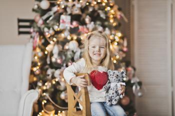 Girl with big red heart on the clothes near the Christmas tree.