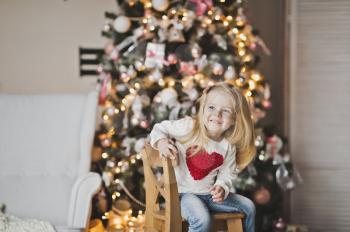 A little girl with a red heart on the clothes sitting in front of the tree.