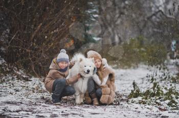 Children on a snowy path playing with the white dog.