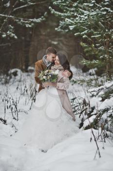 Portrait of newlyweds admiring each other against the background of winter snow-covered dark forest.
