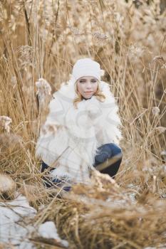Close-up portrait of girl in white furry jacket and hat in the winter among the reeds.