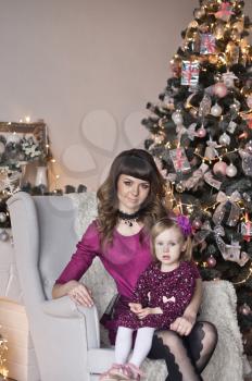 Portrait of baby and mother sitting on a chair near the Christmas tree.