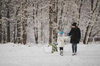 Mother with two children walking on the background of snowy forest.