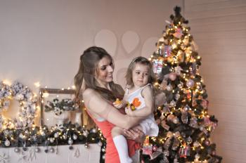 Mom turns her daughter in her arms on the Christmas decorations.