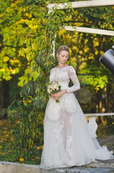 Portrait of a bride in a white dress on background of a garden gazebo entwined with ivy.