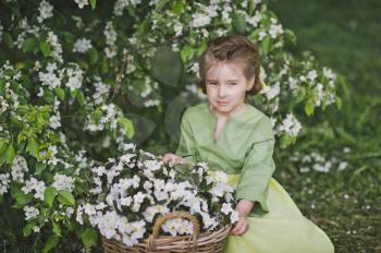 The child is sitting near a big basket of flowers.