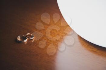 Wedding rings on the varnished table near the lamp.