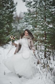 Portrait of a bride in a chic white dress among snow-covered fir branches.