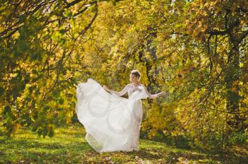 Portrait of a bride in a white dress swirling in the meadow autumn forest.