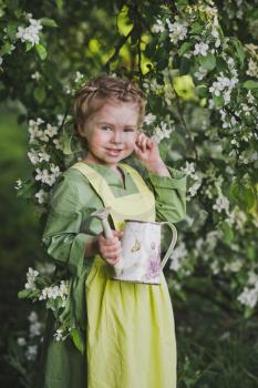 The child with a small watering can in hand walking in the spring garden.