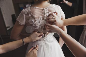 Bridesmaids help the bride to wear a dress.