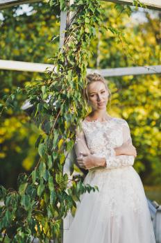 The bride in a slinky dress on a background of an ivy-covered gazebo.