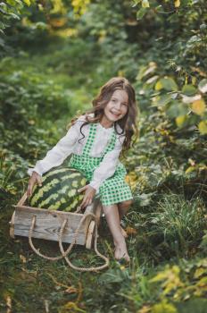 A little girl carries a huge watermelon on a cart.