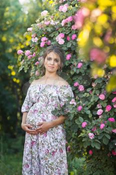 Pregnant beautiful girl standing on the background of a flowering Bush.