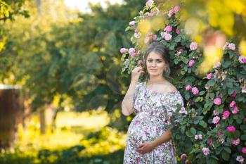 The girl in the position of pregnancy in nature in a free colorful dress.