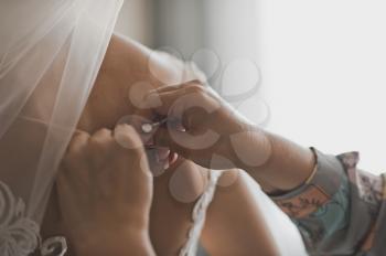 A friend helps the bride to put on a wedding dress.