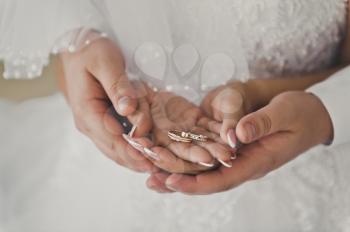 The husband gently embraces the hands of the bride with wedding rings.