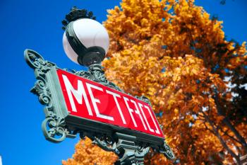 Traditional Paris metro sign with trees in the background. Gold autumn
