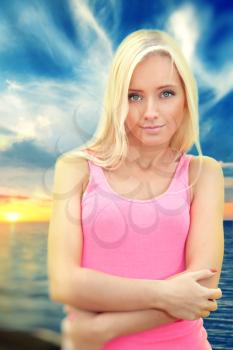 young blond woman standing in the sunset by the sea. summer evening