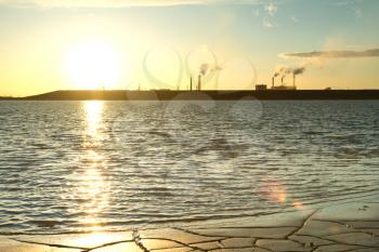 factory smoke from a pipe on a background of lake at sunset