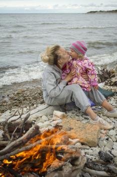 mother and daughter at the sea in the fall sitting around the campfire .