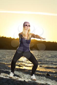 Fitness sport model doing exercises during outdoor work out on sunrise. Beautiful caucasian female training outside on seaside in the morning