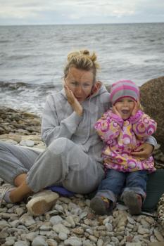 mother and daughter at the sea in the fall sitting around the campfire .