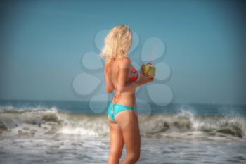 woman in a swimsuit is standing near the ocean with a coconut in her hands. Beach goa